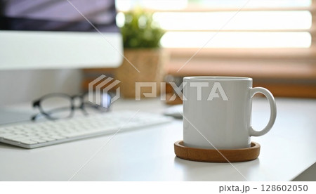 White Mug on Cork Coaster on a Desk with Computer 128602050