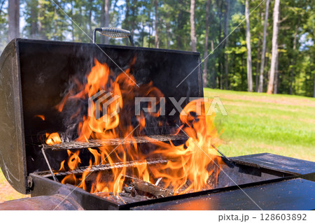 Flames dance from barbecue grill as summer sun shines down in green backyard. 128603892