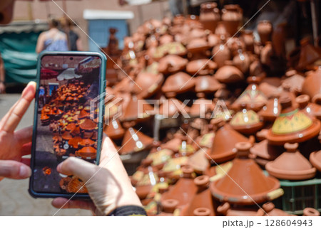 Hand with a mobile phone taking a photo of a set of tagines displayed in street 128604943