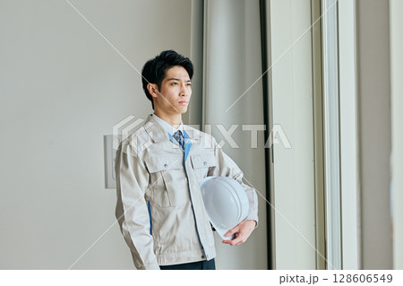 ヘルメットを持つ作業服姿の若い男性 128606549