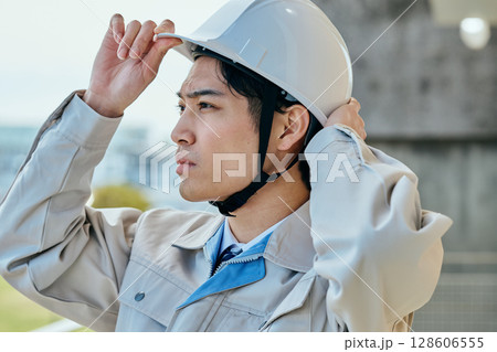 ヘルメットをかぶる作業服姿の若い男性 ヘルメットをかぶる作業服姿の若い男性 128606555