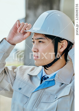 ヘルメットをかぶる作業服姿の若い男性 ヘルメットをかぶる作業服姿の若い男性 128606556