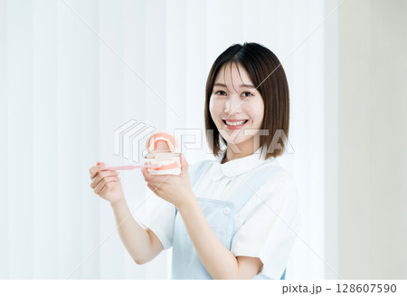 歯ブラシと歯の模型を持つ歯科スタッフの女性 128607590
