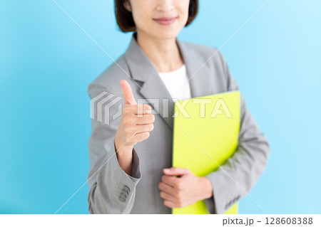 グレーのスーツを着て親指を立てるミドル女性ビジネスウーマン 128608388