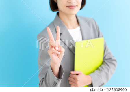 グレーのスーツを着てピースをするミドル女性ビジネスウーマン 128608400