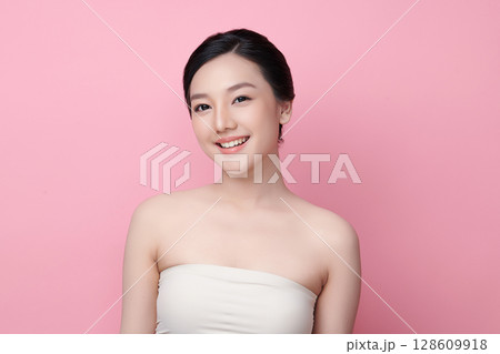 A beautiful young Asian woman with clean, fresh skin against a pink background. Skincare, facial treatment, cosmetology, beauty, and spa. An elegant portrait of an Asian woman. 128609918