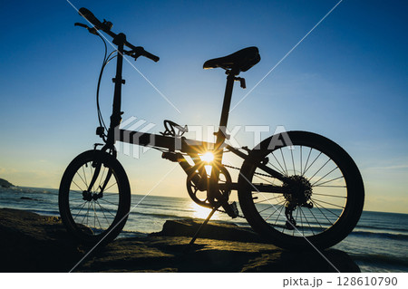 A folding bike on sunrise seaside rocka A folding bike on sunrise seaside rocka 128610790