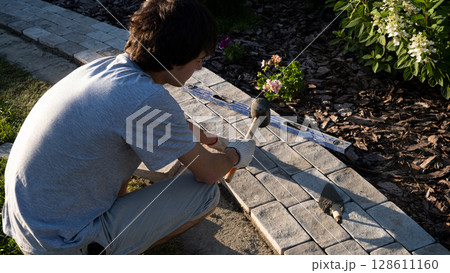 Laying paving stones on cement mortar. Laying a garden path made of tiles. Self-laying of concrete paving slabs in the courtyard of the house. do it yourself. DIY Laying paving stones on cement mortar. Laying a garden path made of tiles. Self-laying of concrete paving slabs in the courtyard of the house. do it yourself. DIY 128611160