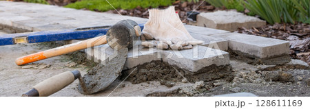Laying paving stones on cement mortar. Laying a garden path made of tiles. banner, Self-laying of concrete paving slabs in the courtyard of the house. do it yourself. DIY 128611169
