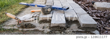 Banner. Laying paving stones on cement mortar. Laying a garden path made of tiles. Self-laying of concrete paving slabs in the courtyard of the house. do it yourself. DIY 128611177