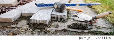 Laying paving stones on cement mortar. banner. Laying a garden path made of tiles. Self-laying of concrete paving slabs in the courtyard of the house. do it yourself. DIY 128611180