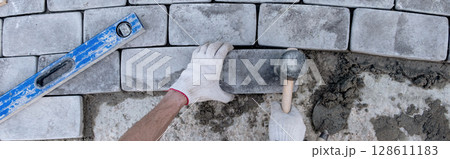 Laying paving stones on cement mortar. Banner. Laying a garden path made of tiles. Self-laying of concrete paving slabs in the courtyard of the house. do it yourself. DIY 128611183
