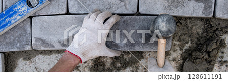 Laying paving stones on cement mortar. banner, Laying a garden path made of tiles. Self-laying of concrete paving slabs in the courtyard of the house. do it yourself. DIY 128611191