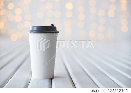 Disposable coffee cup on white wooden surface with soft bokeh light background 128612145