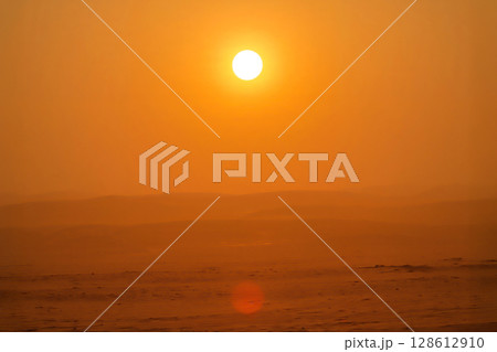 A serene minimalist desert landscape with a bright sun in a warm orange haze. Soft light illuminates vast sand dunes fading into the hazy horizon. 128612910