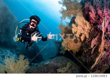 Asian male scuba diver pointing at tropical coral reef in Andaman sea, Thailand. 128614063