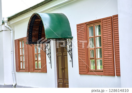 Historic building exterior showcases unique green awning and wooden shutters during daylight 128614810