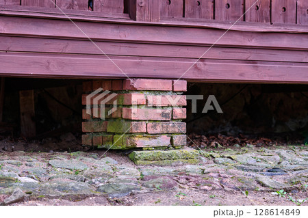 Brick support under wooden structure showing weathered textures and natural elements at a rustic location Brick support under wooden structure showing weathered textures and natural elements at a rustic location 128614849