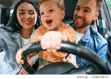 Boy is trying to ride. Family of father, mother and little son are sitting in the modern car 128616613