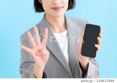スマホを持って4本指を立てるミドル女性ビジネスウーマン 128617049