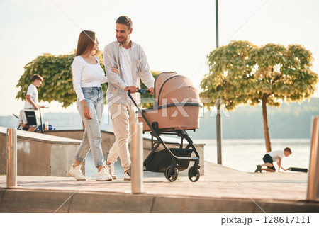 Weekend walk. A young couple with a baby pram are together Weekend walk. A young couple with a baby pram are together 128617111