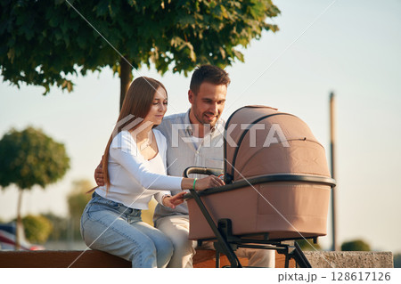 A young couple with a baby pram is walking together A young couple with a baby pram is walking together 128617126