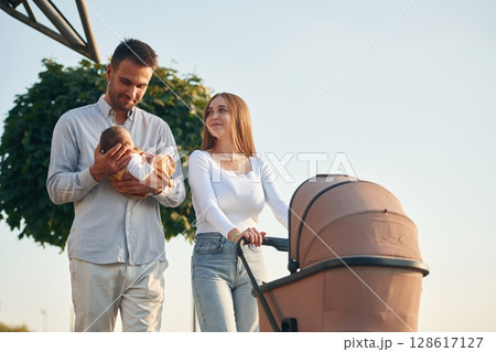 Holding baby in hands. A young couple with a pram is walking together Holding baby in hands. A young couple with a pram is walking together 128617127