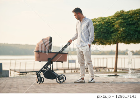 Young father is outdoors, standing with pram Young father is outdoors, standing with pram 128617143