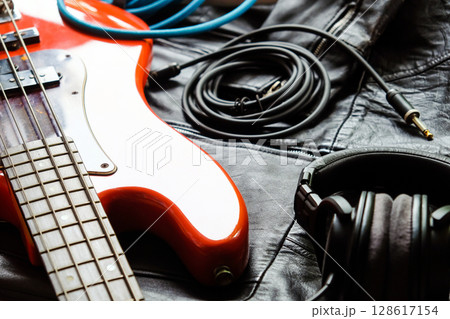 orange electric bass guitar, headphones and cable on a black leather jacket background. 128617154