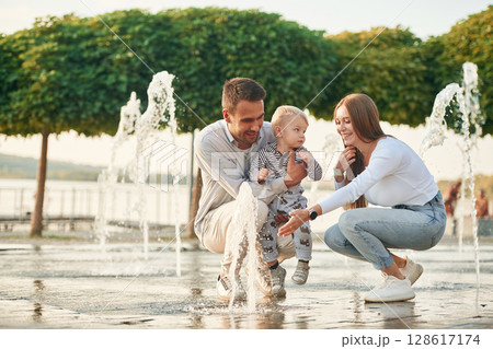 Mother and father are playing with their son in the fountains in the park Mother and father are playing with their son in the fountains in the park 128617174