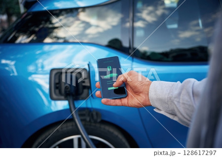 Showing process on the display of smartphone. Man with blue electric car on the charge station 128617297