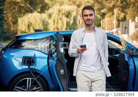 Front view. Man with blue electric car on the charge station Front view. Man with blue electric car on the charge station 128617304