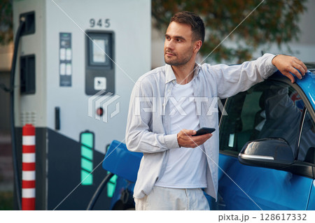 Standing and waiting for process finished. Man with blue electric car on the charge station 128617332