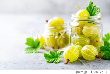 Gooseberry fruit in glass jar with fresh green leaves on gray surface showing processed agriculture export concept with natural healthy food and bright fresh colors Gooseberry fruit in glass jar with fresh green leaves on gray surface showing processed agriculture export concept with natural healthy food and bright fresh colors 128617405