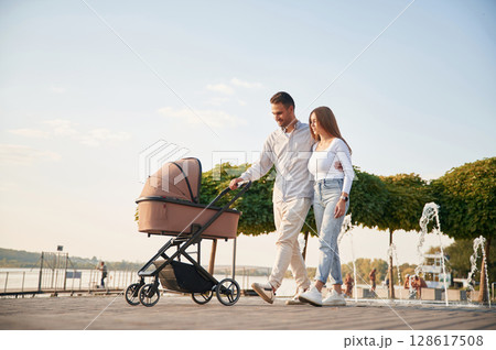 Happy family outdoors. A young couple with a baby pram is walking together 128617508