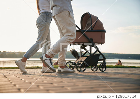 View from below of legs. A young couple with a baby pram is walking together View from below of legs. A young couple with a baby pram is walking together 128617514