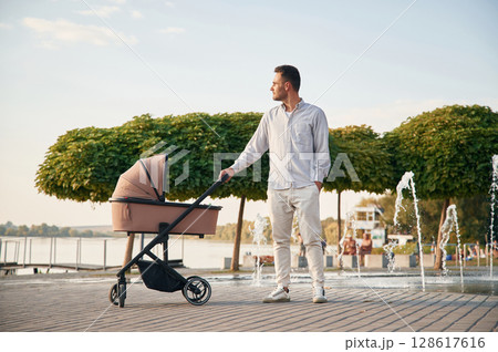 Young father is outdoors, standing with pram Young father is outdoors, standing with pram 128617616