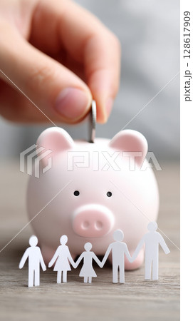 Family saving money by putting coin into piggy bank symbolizes budget planning and financial security for future with care and hope 128617909