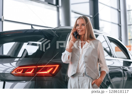 Conversation by the phone. Woman in formal clothes is in the car dealership 128618117
