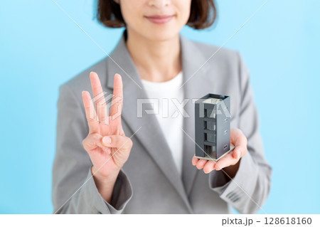 オフィスビルの模型を持って3本指を立てるミドル女性ビジネスウーマン 128618160