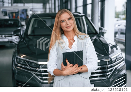 With tablet in hands. Woman in formal clothes is in the car dealership With tablet in hands. Woman in formal clothes is in the car dealership 128618191