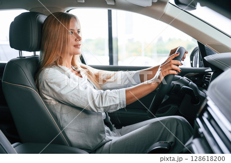Side view. Woman is sitting in a car and driving it Side view. Woman is sitting in a car and driving it 128618200