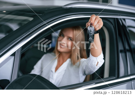Keys from new car. Woman in formal clothes is indoors in the auto salon Keys from new car. Woman in formal clothes is indoors in the auto salon 128618213