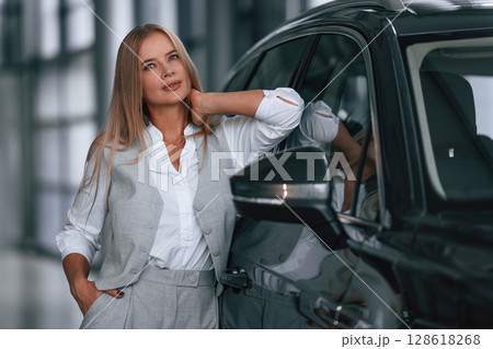 Leaning on the automobile. Woman in formal clothes is in the car dealership 128618268