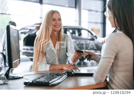 Giving the keys. Female manager is helping woman customer in the car dealership salon Giving the keys. Female manager is helping woman customer in the car dealership salon 128618294