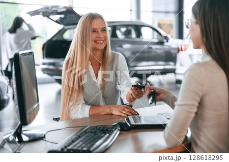 Giving the keys. Female manager is helping woman customer in the car dealership salon 128618295