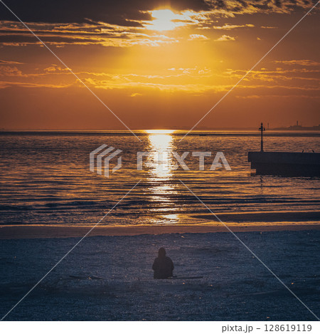 夕日に照らされてオレンジに輝く海を背景にしたシルエットの人物 128619119