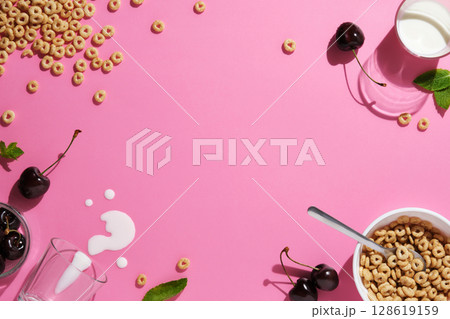 Grain rings, cherries, mint leaves, a spoon, spilled milk, and a bowl on pink background. A breakfast concept with space for your text. 128619159