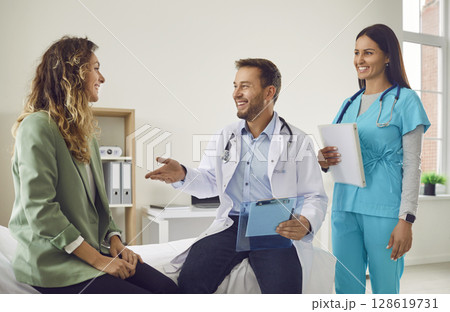 Woman talking with man doctor and nurse holding report file with appointment sitting in clinic. Woman talking with man doctor and nurse holding report file with appointment sitting in clinic. 128619731