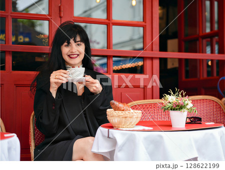 Smiling woman holding coffee at a Paris street cafe 128622199